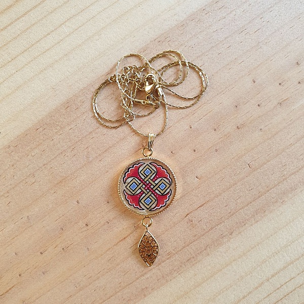 Halskjede anheng belyst med bl&aring; palmetter, gull og r&oslash;d sammenfletting p&aring; gullkjede